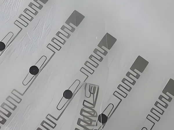 Clear UHF RFID labels showing the inlay inside, each an antenna with the chip area at its centre; one is partly peeled from the film