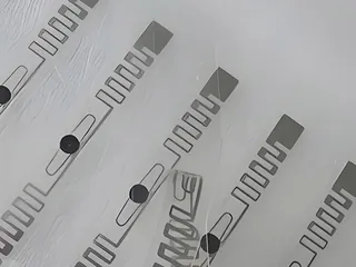 Clear UHF RFID labels showing the inlay inside, each an antenna with the chip area at its centre; one is partly peeled from the film